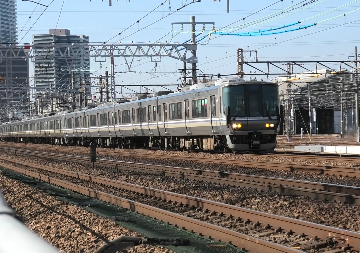 安満遺跡公園ぞいを走る新快速と、その奥にある車両基地の建屋