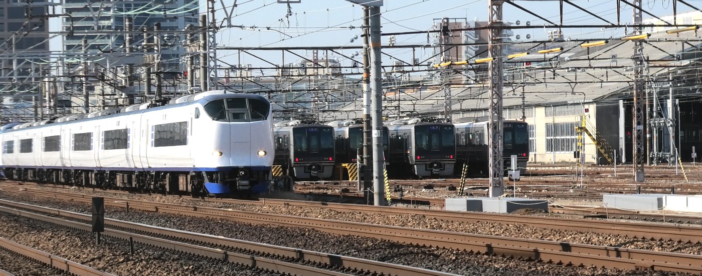特急はるかが走るその奥に、車庫で休む電車が何本も並んでいる