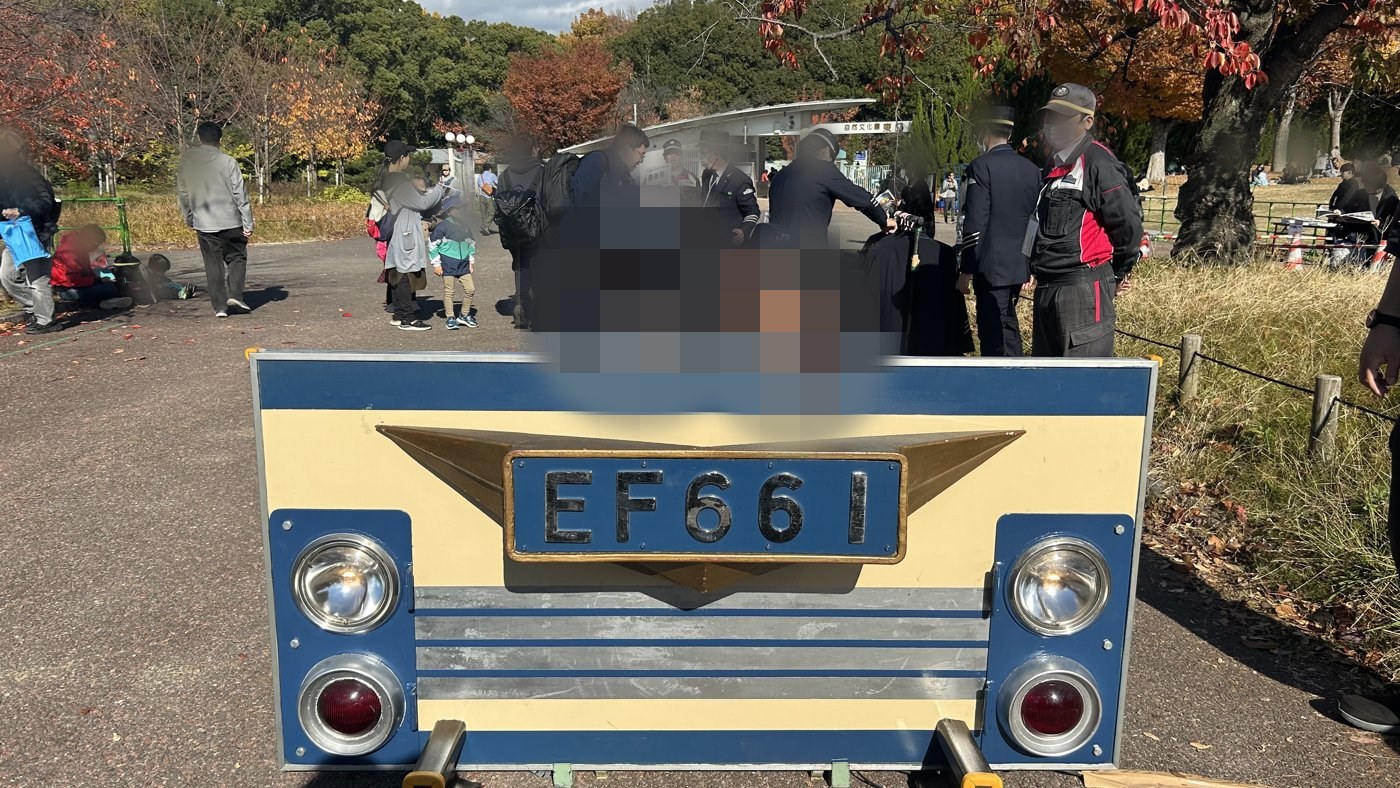 万博鉄道まつり2025で、EF66 1のナンバープレート付きカットパネルの前で制服・制帽姿で記念撮影する兄弟