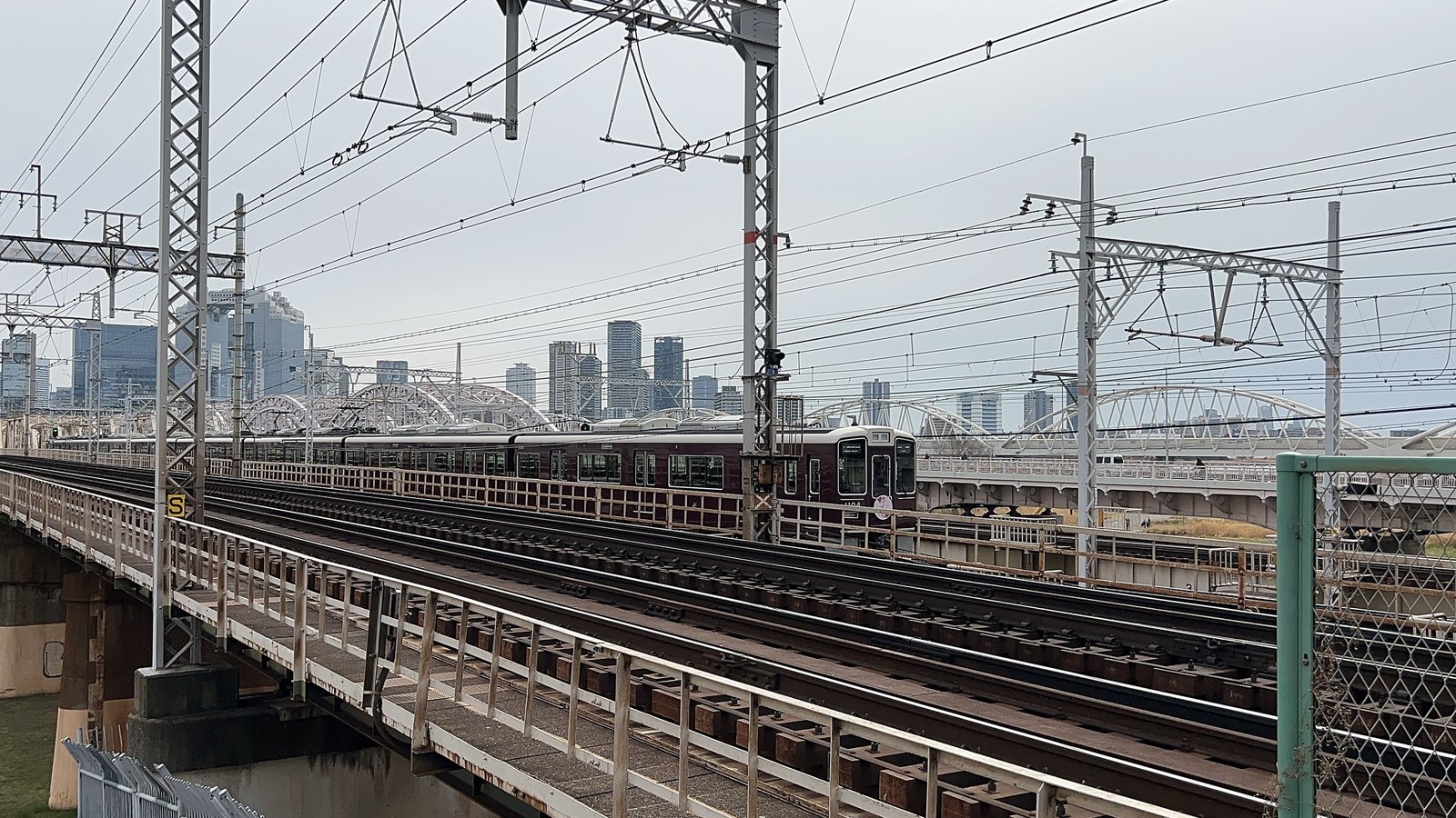 京都線側から見た、淀川の鉄橋を渡る阪急電車。奥にアーチ橋と大阪のビル群