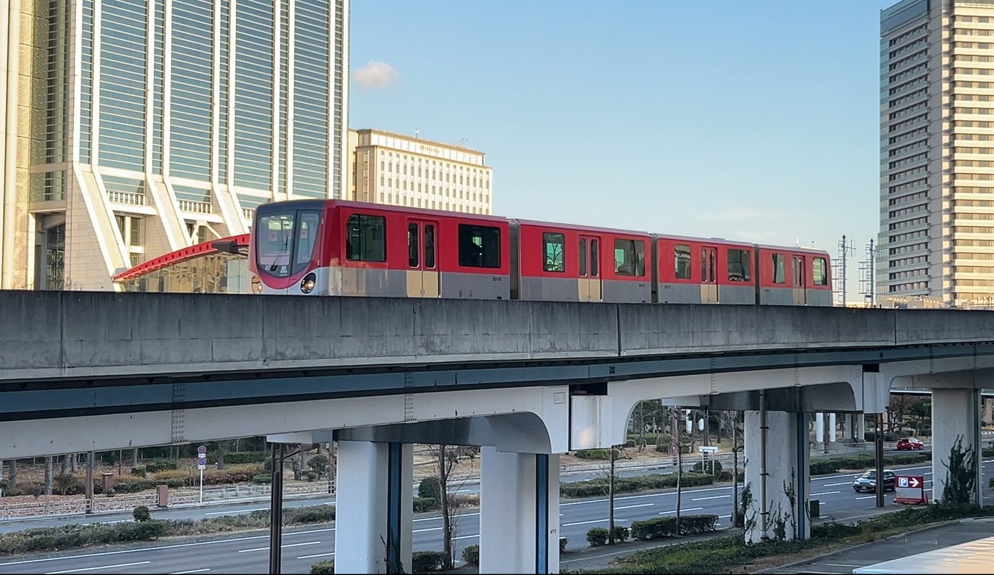 トレードセンター前駅の赤いアーチをバックに走る赤いニュートラム